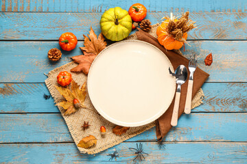 Halloween table setting with pumpkins, autumn leaves and spiders on blue wooden background