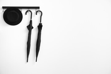 Hanger with black umbrellas and hat on light wall