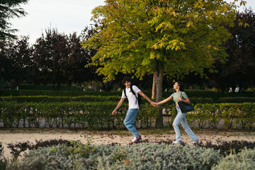 Naklejka na ściany i meble Pair of college students running together to university. They are smiling and holding hands while they run and hold their backpacks.