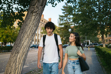 Pair of students college leaving the university while they talk. She looks at him while smile.