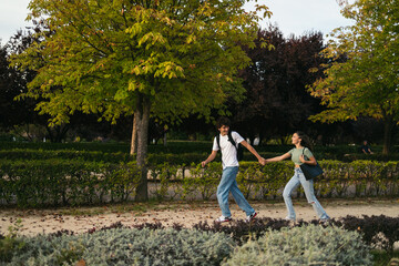 Fototapeta premium Pair of college students running together to university. They are smiling and holding hands while they run and hold their backpacks.