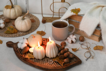 Composition with burning candles, cup of tea and autumn decor on light table