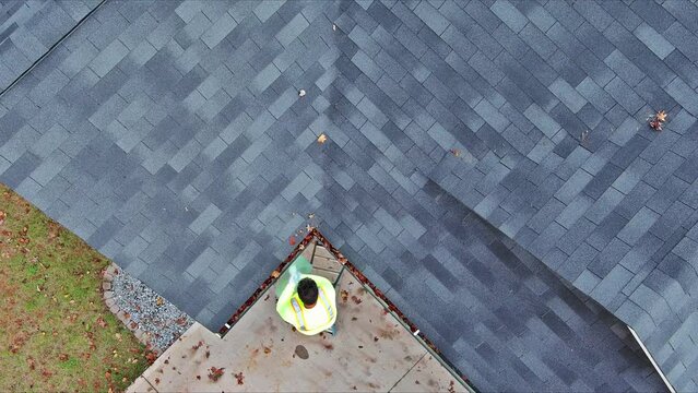 There is worker cleaning clogged roof gutter drain which has been clogged with dirt, debris, fallen leaves.