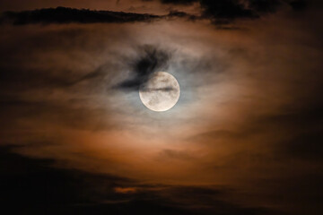Full moon on a cloudy night. Natural colored clouds around the Moon in the sky are an optical effect caused by the refraction of moonlight from ice crystals in the upper atmosphere
