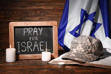 Chalkboard with text PRAY FOR ISRAEL, candles, military cap, Torah and flag on wooden table