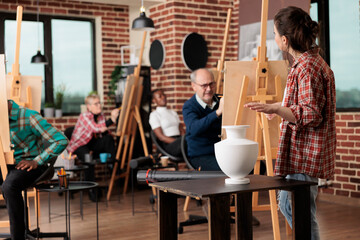 Group drawing classes. Young woman artist teaching art to people from all age groups, female teacher explaining how to draw vase with pencil, art team building activities concept
