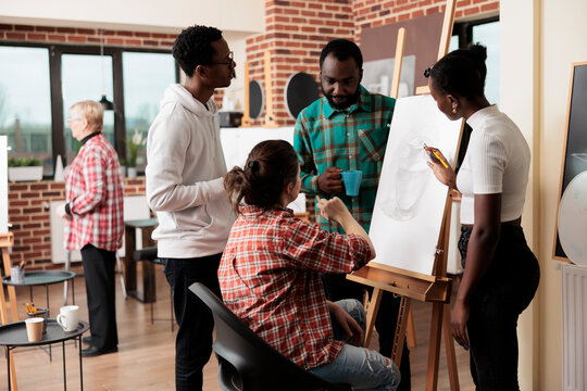 Young people friends taking drawing class in art studio, attending creative workshop together. Group of African American students men and women listening to teacher, learning sketching techniques