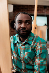 Naklejka premium Creativity and self expression through art. Portrait of African American guy sitting at easel exploring creativity with drawing lessons, smiling young black man visiting painting class for adults