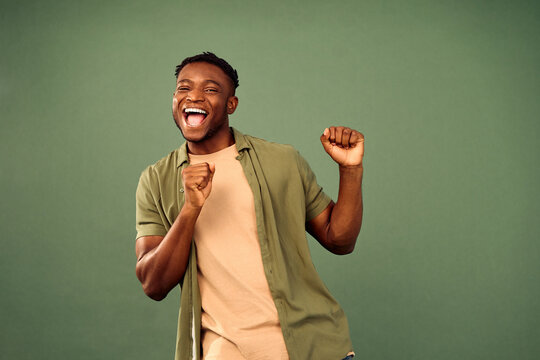 Leisure with fun. Energetic african american gun in casual wear actively dancing with flexible body over green studio background. Joyful young man having fun while perfectly feeling music beat.