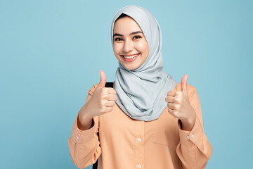 Young smiling happy arabian asian muslim woman in abaya hijab clothes showing thumb up like gesture isolated on plain blue background studio portrait People middle eastern islam religious concept - obrazy, fototapety, plakaty