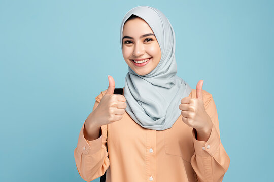Young smiling happy arabian asian muslim woman in abaya hijab clothes showing thumb up like gesture isolated on plain blue background studio portrait People middle eastern islam religious concept