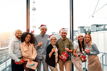 Happy cheerful smiling group of business people celebrating a corporate party in the office on New Year's Eve. A team of various handsome men and women are holding gifts and drinking champagne.