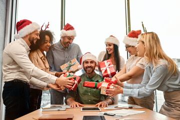 There are not many gifts. A group of business colleagues in Santa hats are giving Christmas gift...
