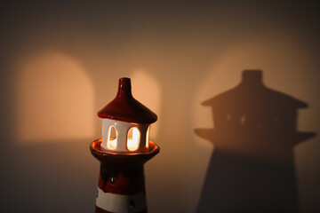 burning candle in a candlestick in the shape of a lighthouse with a shadow, cozy warm atmosphere