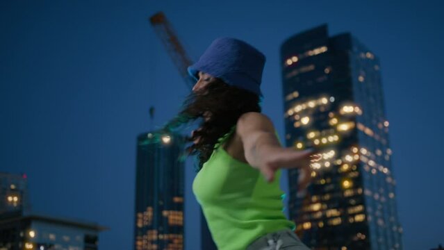 Smiling sexy girl moves hands making her long curly hair fly 4K. Portrait shot of beautiful and happy African American girl dancing at night street of cosmopolitan modern city on urban background 4K