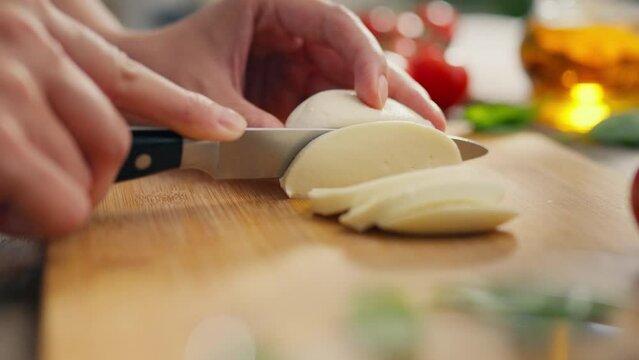Basil leaf. Housewife happily slicing mozzarella at her home kitchen workplace. Close-up of expectant mother cutting a piece of cheese with a knife new methods of preparing fresh snacks, caprese toast