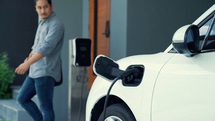 A man unplugs the electric vehicle's charger at his residence. Concept of the use of electric...