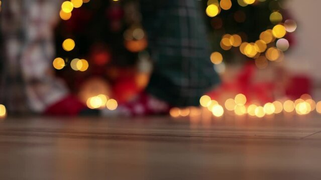 Two Pairs Of Legs In Christmas Pajamas Hugging Near Decorated Christmas Tree, Women's Feet Tiptoe To Reach Out To Kiss Loved One. Concept Of Family Love Christmas And New Year. Unrecognizable Couple