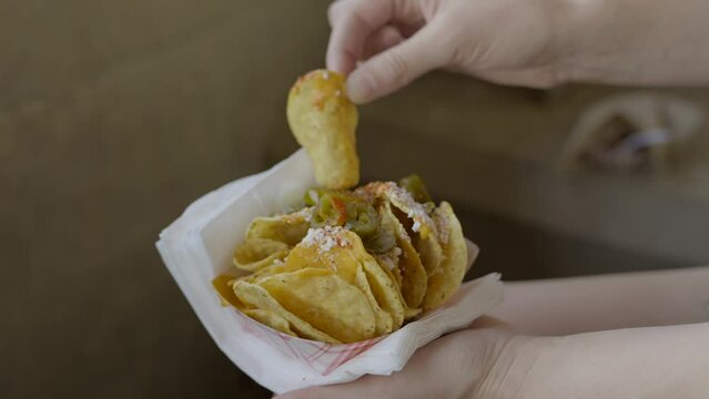 This video shows a close up view of a hand grabbing concession cheese nachos in slow motion.