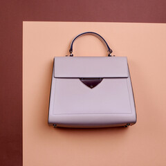 Fashionable beige leather female top-handle bag with black trim, metal accent, and feet isolated on...