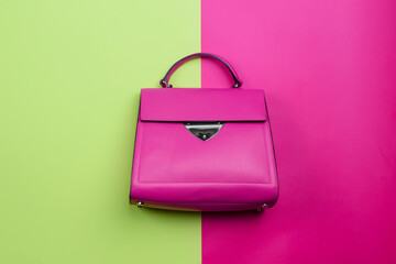 Modern female top-handle bag in fuchsia leather with a black trim accent, a silver metal detail, and feet isolated on a bright contrasting background with copy space. Fashion blog or magazine concept.