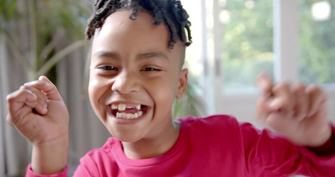 Portrait of happy african american boy with missing teeth dancing in sunny room, slow motion
