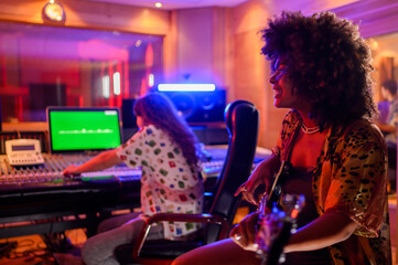 A multiracial bass player smiling and playing bass, recording session in a music studio.