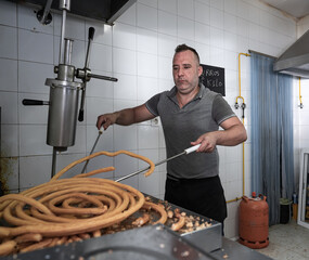 Cocinero sacando masa frita con los palos de churrero para hacer los churos. Los churros son un dulce frito típico español para desayunos y meriendas.