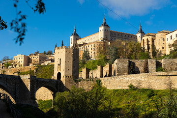 Obraz premium Impressive view of ancient Alcazar of Toledo palace and Alcantara bridge over Tagus river, at capital of province of Toledo in central Spain