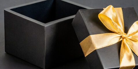 blank open black gift box or opened black present box with gold ribbons and bow isolated on