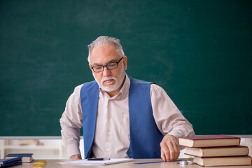 Old male teacher in front of green board