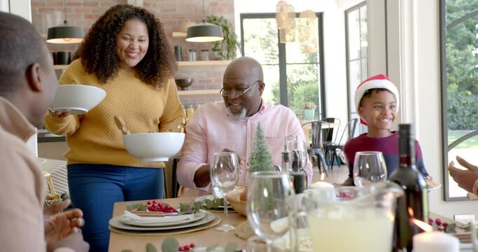 Happy african american mother serving dishes to multi generation family at christmas dinner table
