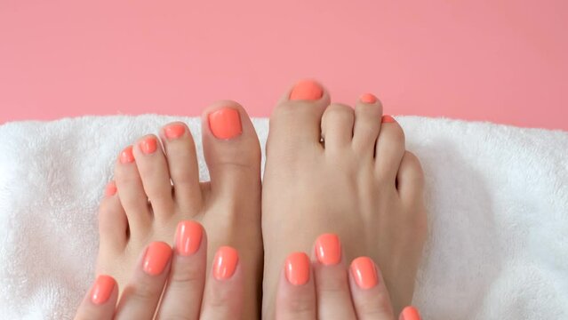 Female hands and feet with manicure and pedicure on towel and pink background close-up, top view.