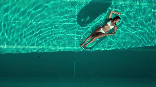 Beautiful sunkissed woman relaxing in a pool - top down aerial view