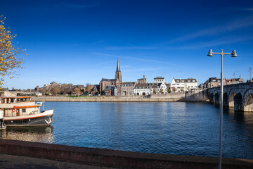 Fototapeta premium Panorama of the Maastricht Waterfront on the Meuse Maas river with a focus on the Sint Martniuskerk, a catholic church, and the saint servatius bridge over the Maas meuse River.