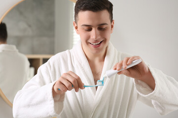 Happy man squeezing toothpaste from tube onto toothbrush in bathroom