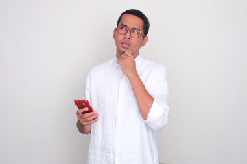 Adult Asian man thinking about something while holding mobile phone