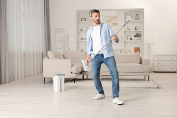 Happy man in headphones having fun with mop while cleaning at home