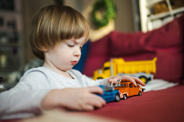 Cute toddler boy playing with toy cars. Small child having fun with toys. Kid spending time in a cozy living room at home.