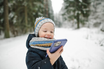 Cute toddler boy having fun on a walk in snow covered pine forest on chilly winter day. Child exploring nature.
