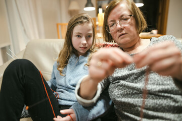 Grandmother and teenage granddaughter knitting on a sofa. Grandma teaching teen child to knit.
