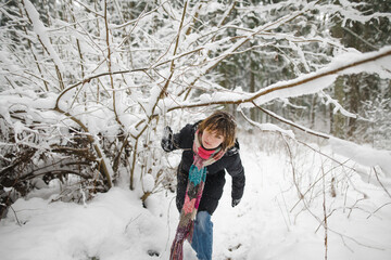 Cute teen girl having fun on a walk in snow covered pine forest on chilly winter day. Teenage child exploring nature.