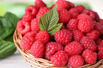 Tasty ripe raspberries and green leaf in basket on table, closeup