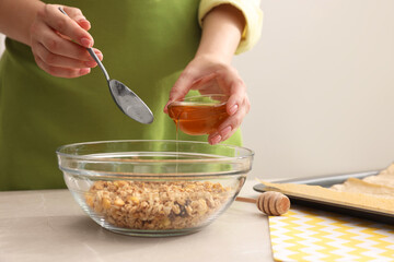 Making granola. Woman adding honey into bowl with mixture of oat flakes and other ingredients at...