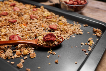 Making granola. Baking tray with mixture of oat flakes, other ingredients and spoon on table,...
