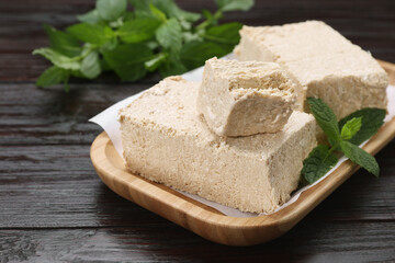 Pieces of tasty halva and mint on wooden table, closeup