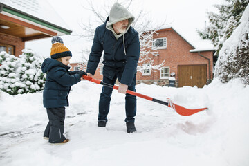 Adorable toddler boy helping his grandfather to shovel snow in a backyard on winter day. Cute child...