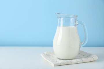 One jug of fresh milk on white table against light blue background, space for text