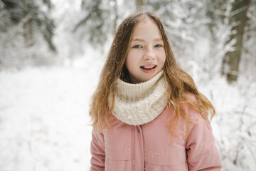 Cute teen girl having fun on a walk in snow covered pine forest on chilly winter day. Teenage child exploring nature.