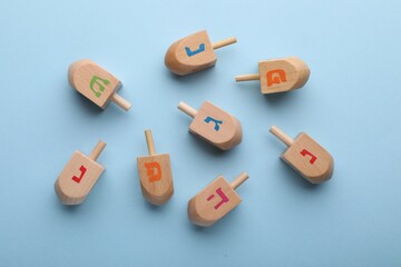 Wooden dreidels on light blue background, flat lay. Traditional Hanukkah game